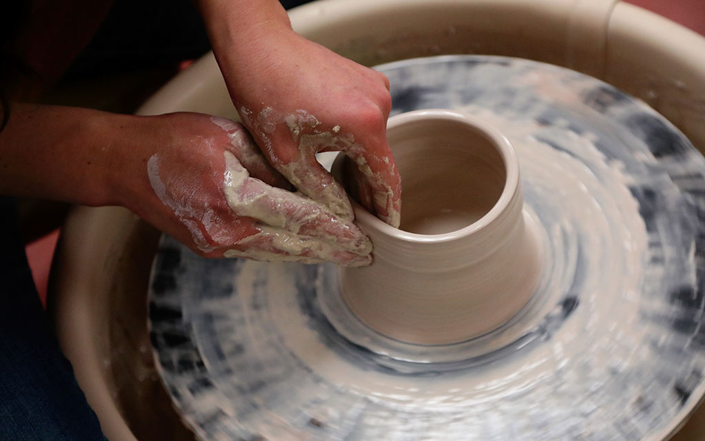 Two hands molding clay on a potter's wheel.
